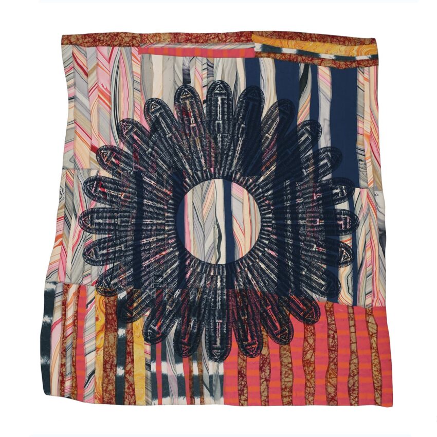 Colorful quilt with a large black circular pattern and various geometric designs in shades of red, blue, and yellow.