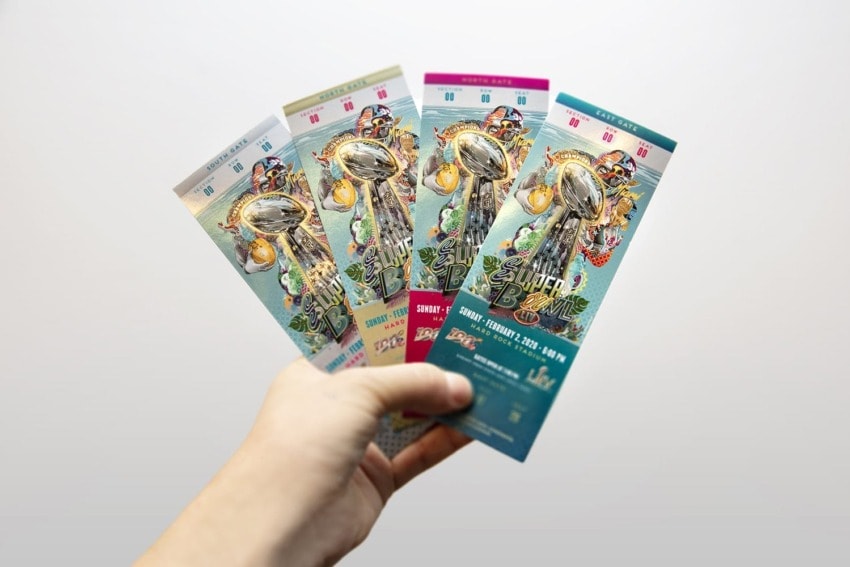 Hand holding four colorful Super Bowl tickets with trophy illustrations and event details.