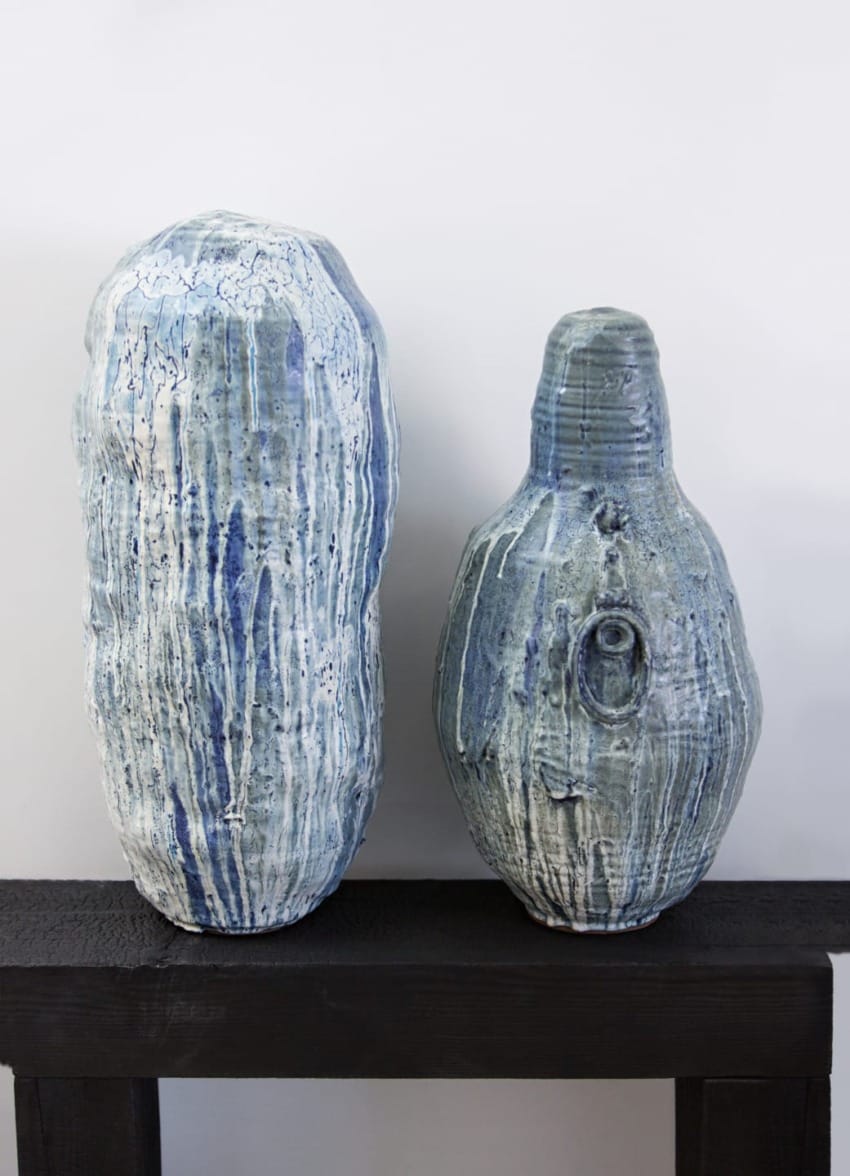 Two tall, textured ceramic vases with blue glaze on a black wooden shelf against a plain white background.