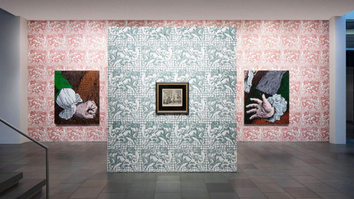 Art exhibit featuring two hand-themed paintings on patterned walls and a framed central artwork in a modern gallery setting.