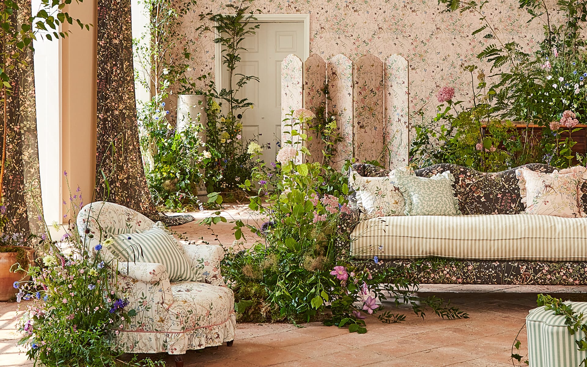 Floral-themed living room with patterned furniture, lush green plants, and a white door in the background.