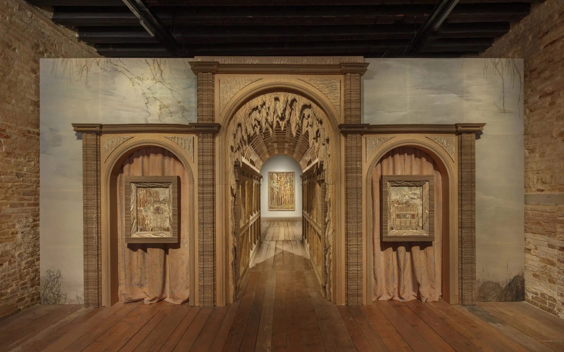 Wooden archway with framed art, leading to a corridor with artwork at the end, set in a gallery with textured walls.