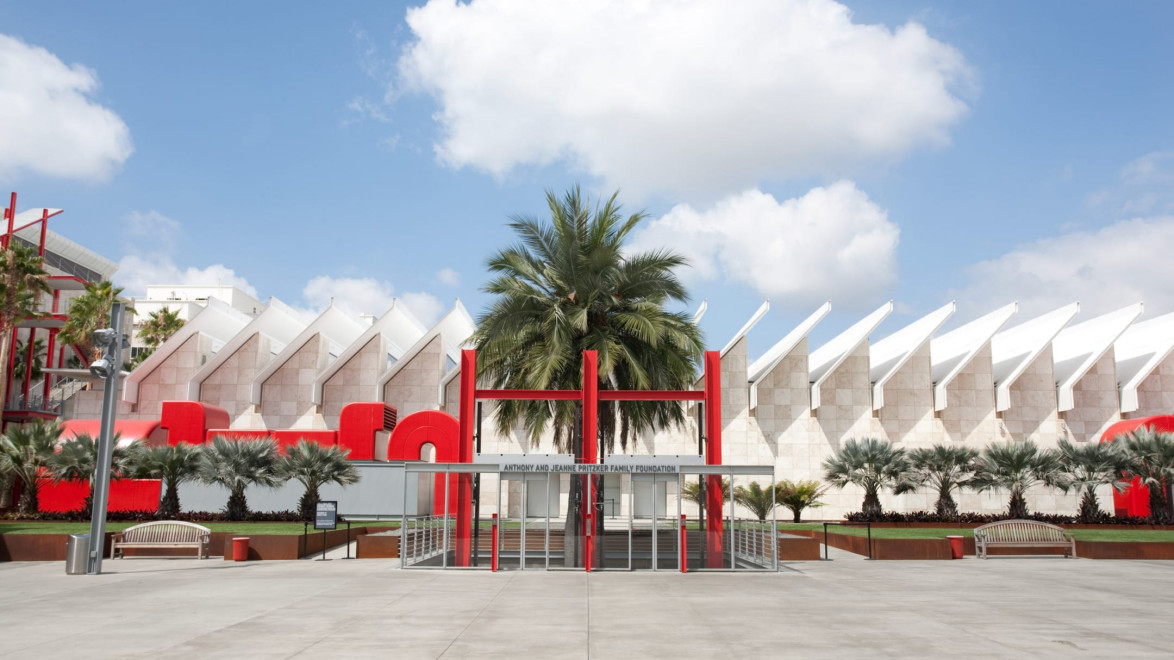 Modern art museum exterior with geometric architecture, red accents, palm trees, and a bright blue sky with scattered clouds