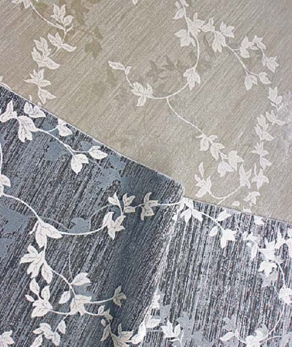 Textured wallpaper samples in beige and gray with white vine and leaf patterns, displayed against a simple backdrop.