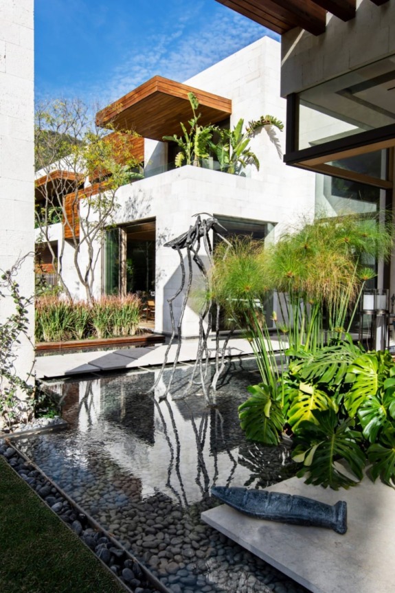 Modern house with lush greenery and a reflective water feature in the courtyard under a clear blue sky.