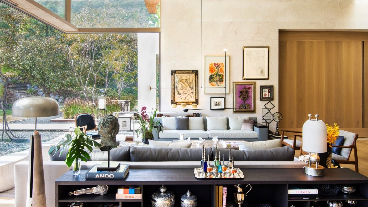 Modern living room with large windows, art-filled walls, and stylish decor overlooking a garden.