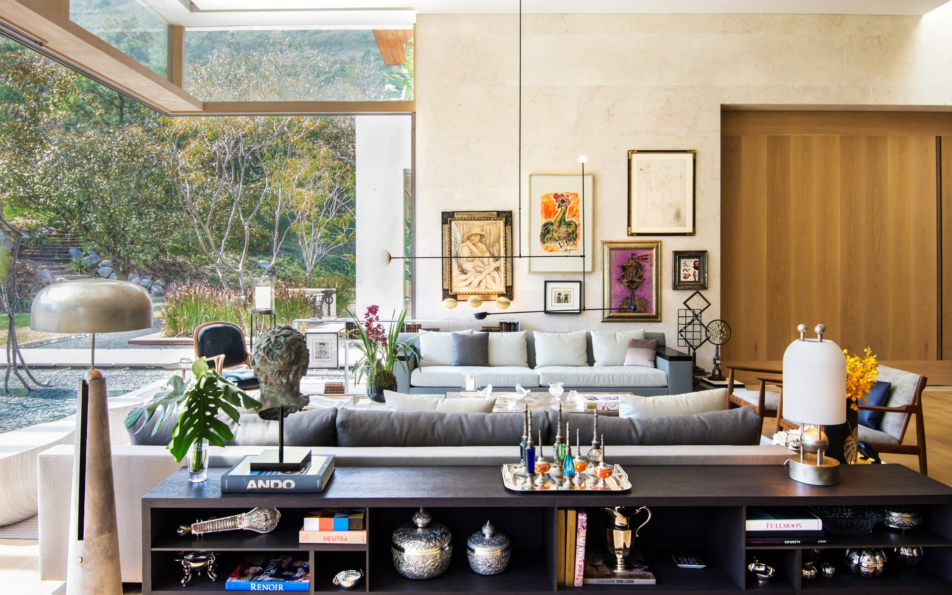 Modern living room with large windows, art-filled walls, and stylish decor overlooking a garden.