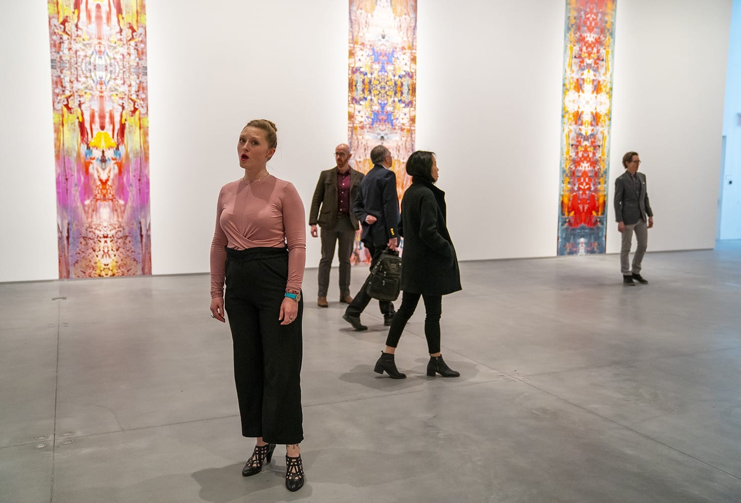 Visitors explore a modern art gallery with colorful vertical paintings on display.