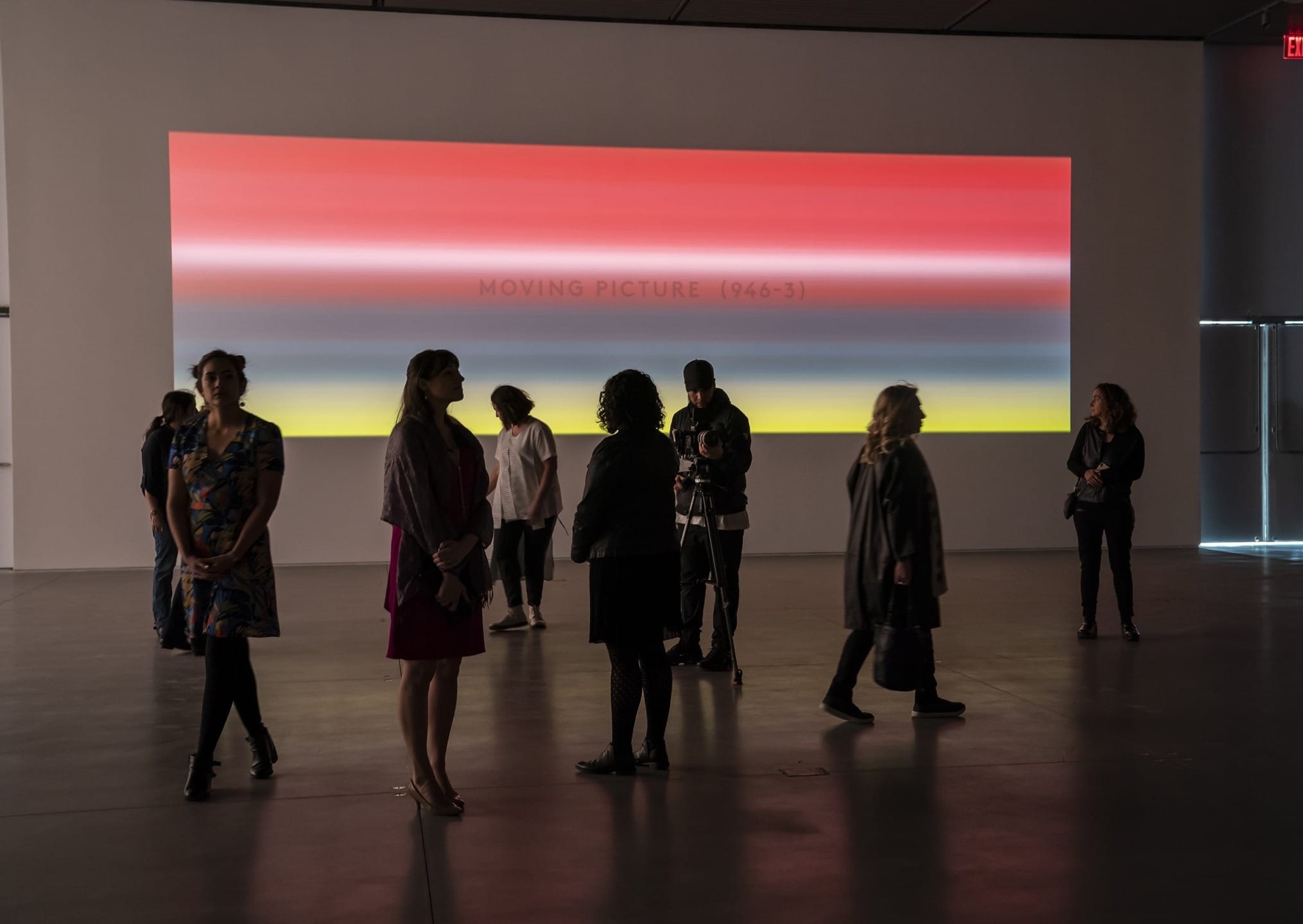 People viewing a colorful, striped digital artwork titled "Moving Picture (946-3)" projected on a gallery wall.