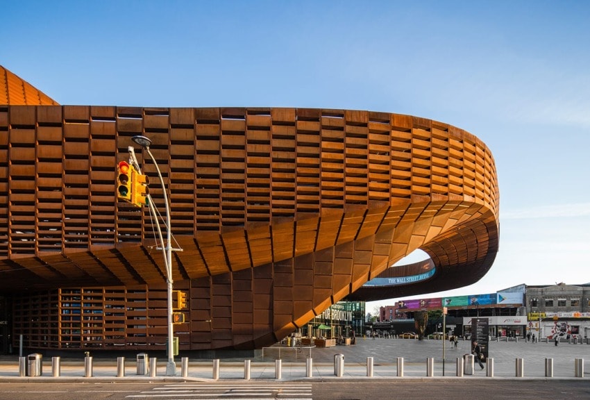 Modern curved building facade with unique architectural design featuring rust-colored panels under a clear blue sky