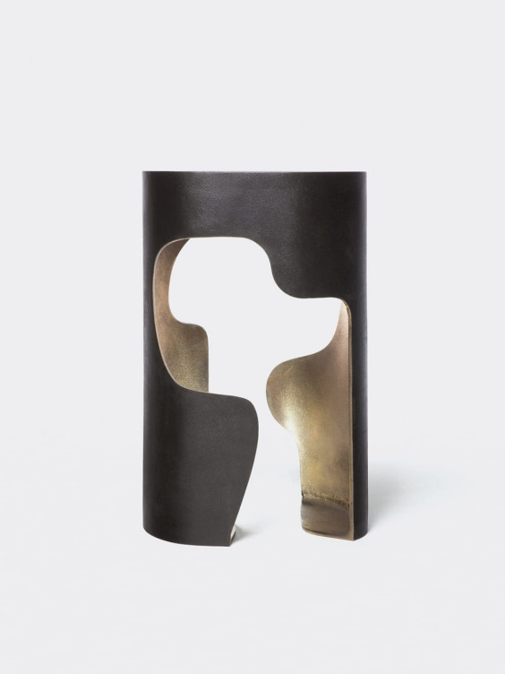 Abstract black and bronze sculpture with curved, cut-out shapes against a plain white background.