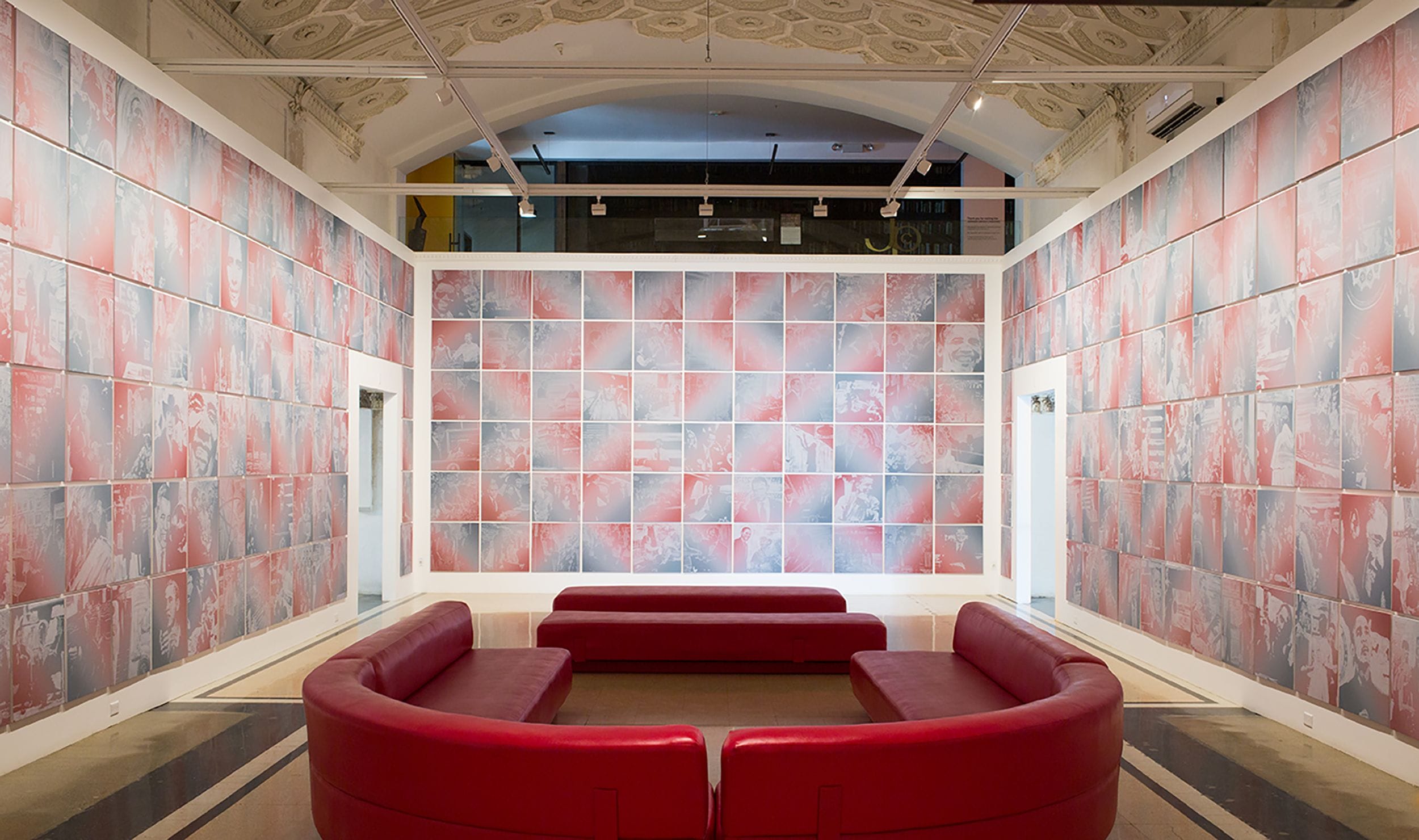 Art gallery room with red and gray wall art, ornate ceiling, and maroon semi-circular benches in the center.