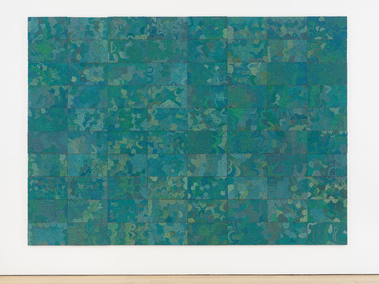 Abstract art piece with green and blue mosaic patterns displayed on a white wall at an art gallery.