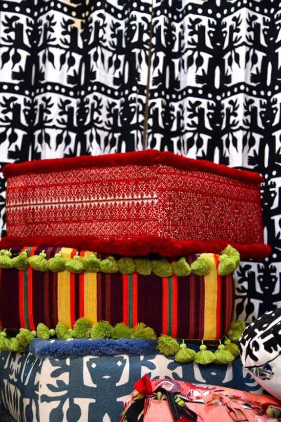 Stack of colorful cushions with intricate designs and tasseled edges against a bold black and white patterned background.