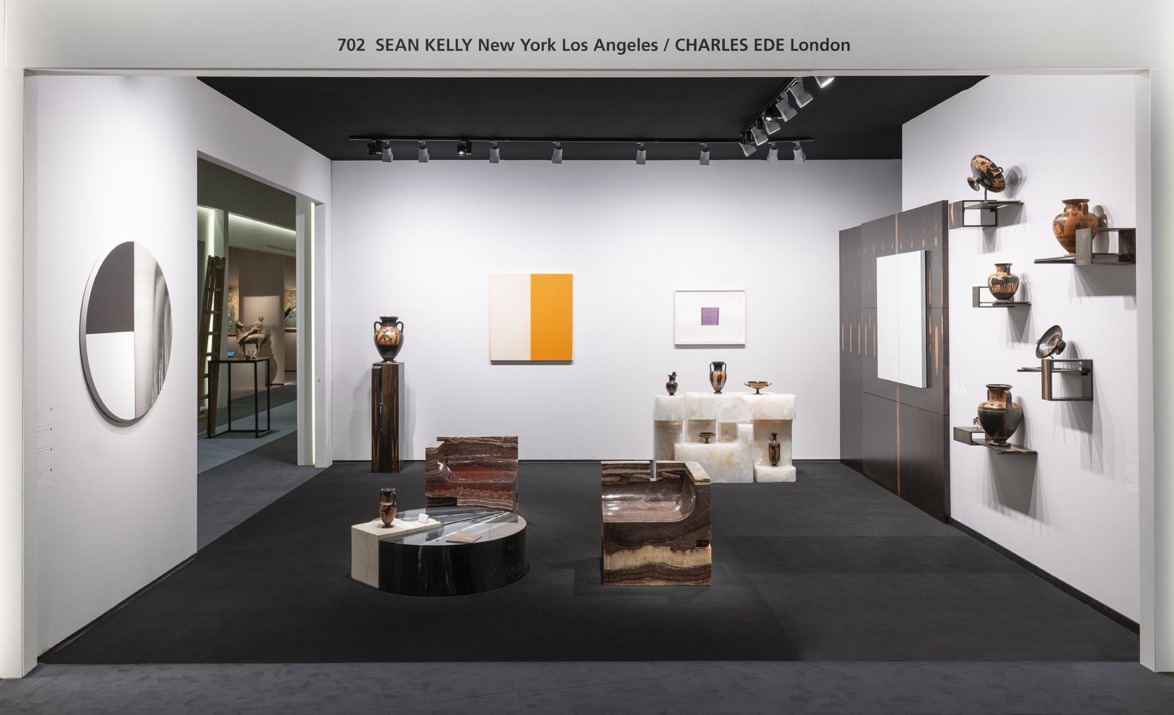 Art gallery exhibit with modern art pieces, including sculptures and paintings, displayed on black and white walls.