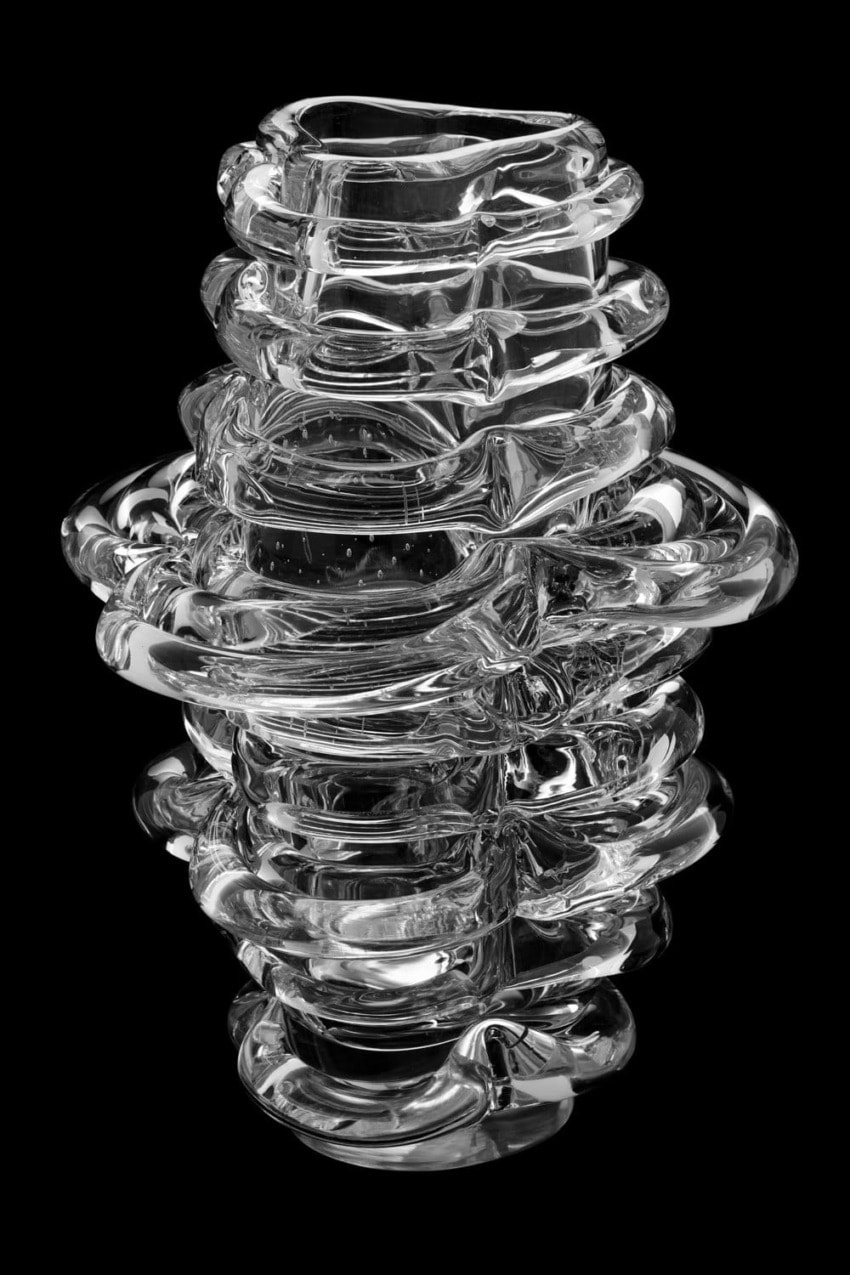 Abstract clear glass sculpture with layered, swirling design against a black background.
