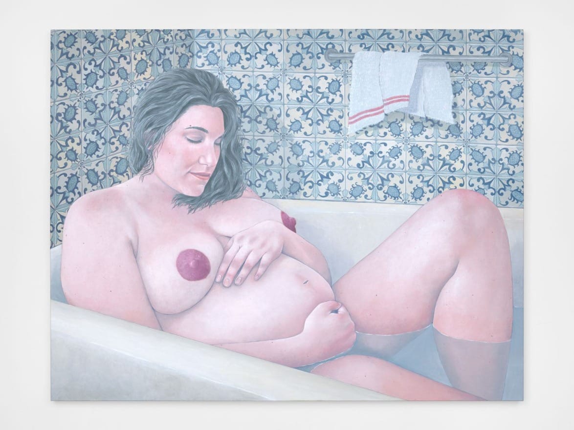 Pregnant woman relaxing in a bathtub surrounded by decorative blue tiled wall with a towel hanging nearby.