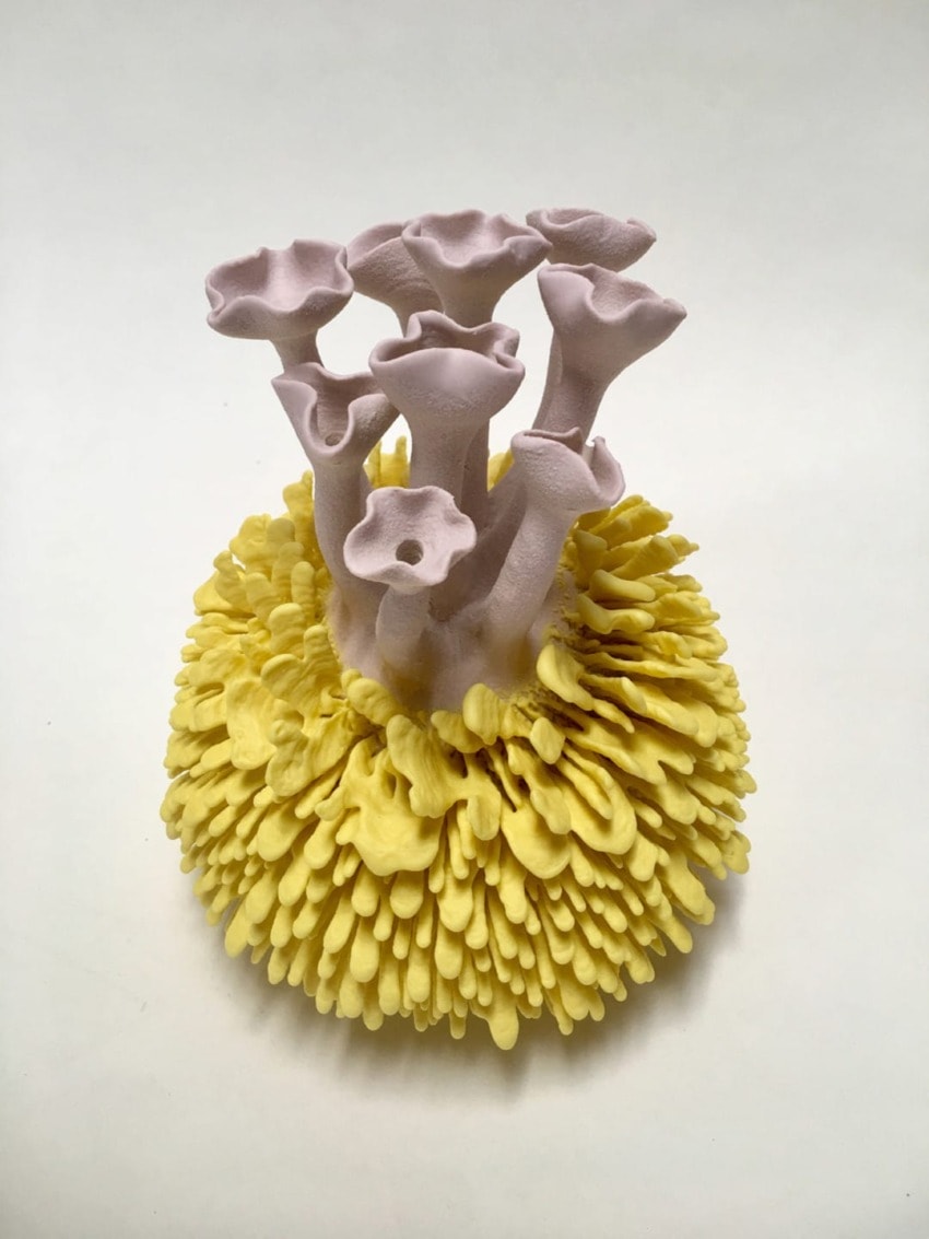 Sculpture resembling coral with yellow base and pink tubular structures against a white background.