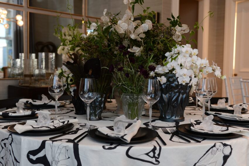 Elegant dining table with artistic tablecloth, white orchids, and swirling wine glasses set for a sophisticated gathering.