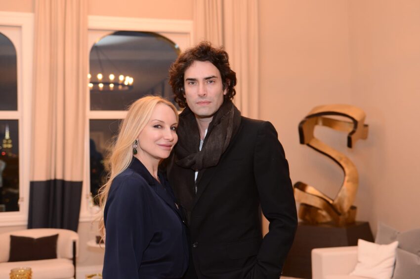 A couple posing indoors in a stylish living room with modern decor and large windows.