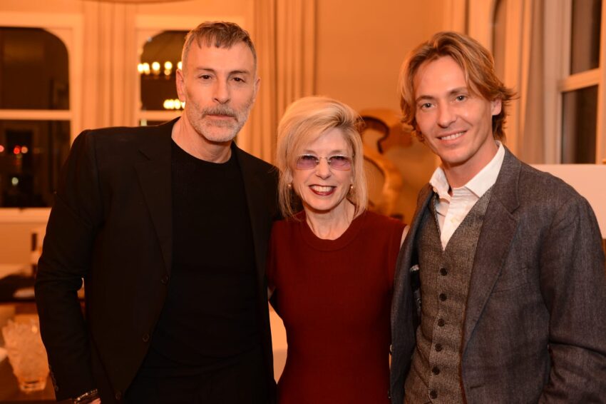 Three people smiling and posing together at an indoor event in a warmly lit room.