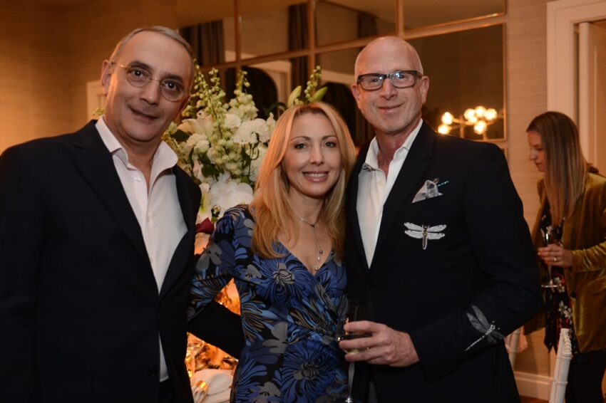 Three people posing for a photo at a social event, with a floral arrangement in the background.