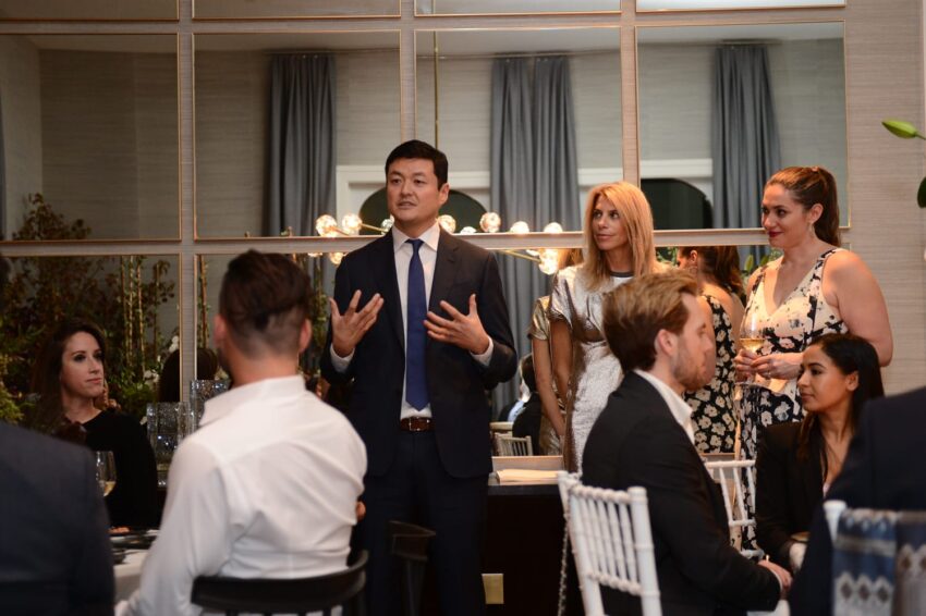 Person in a suit speaking to a seated audience at a formal event.