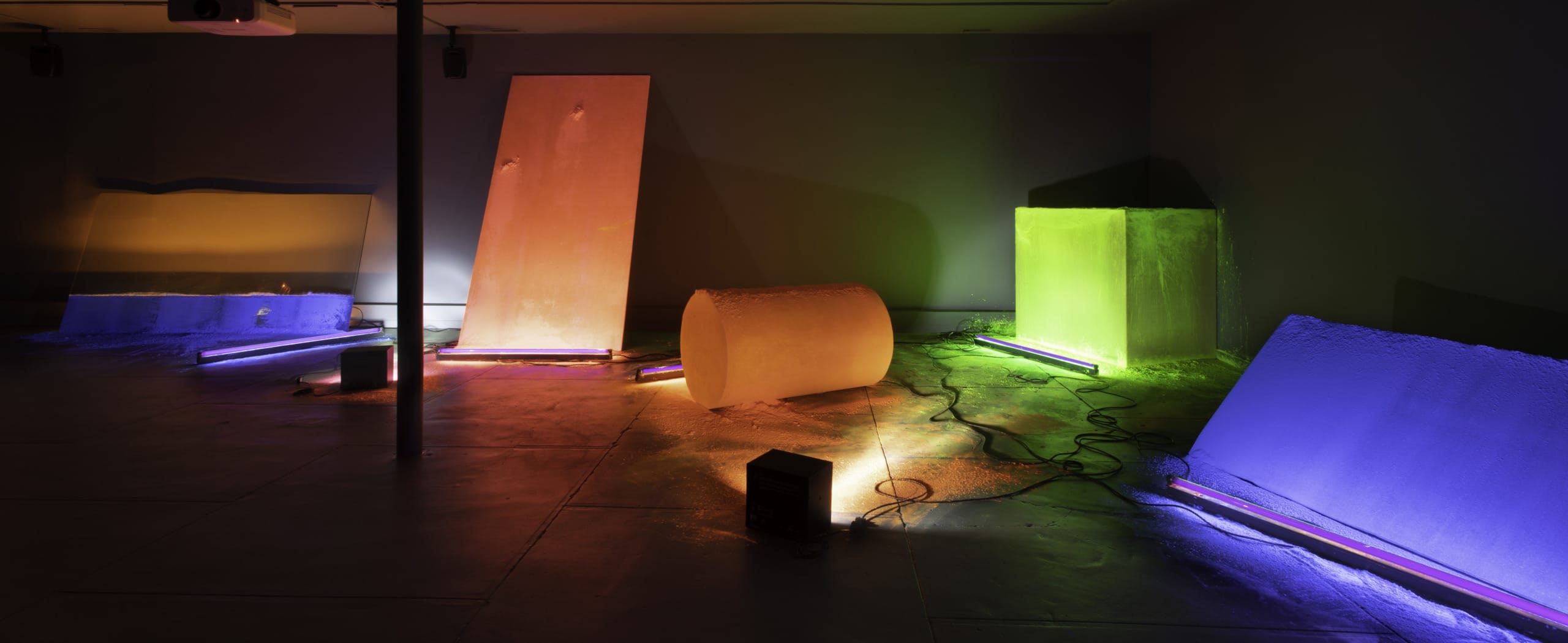 Colorful geometric sculptures with neon lights in a dimly lit art gallery exhibit.