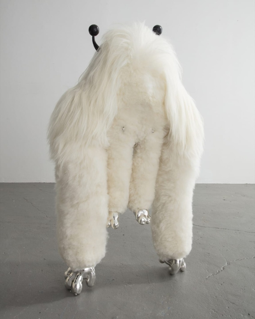Fluffy white sculpture resembling an imaginative creature with metal feet on a grey floor in a minimalist room.