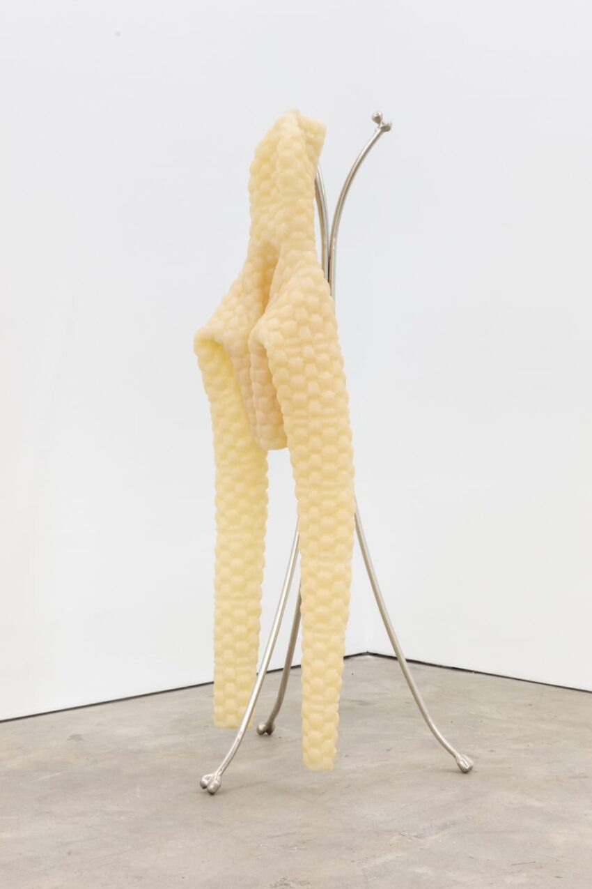 Abstract yellow sculpture on a silver metal stand placed in a minimalist white and gray room.
