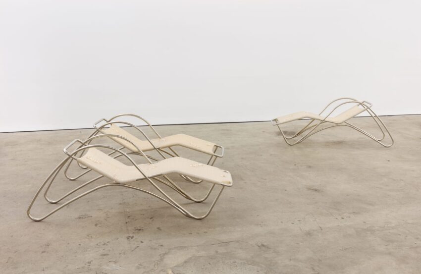 Contemporary metal and fabric lounge chairs on a concrete floor in a minimalist setting.