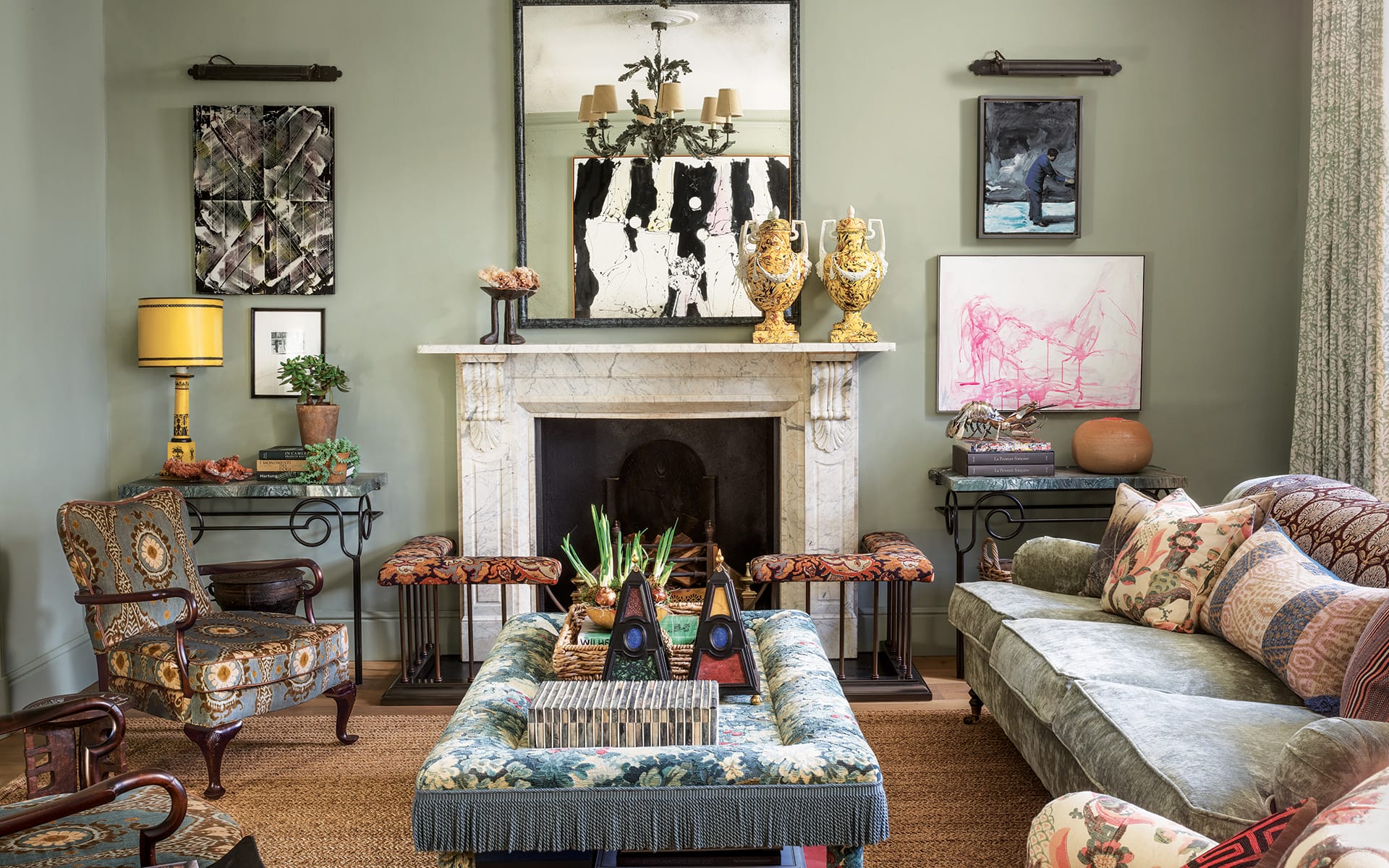 Eclectic living room with green walls, ornate fireplace, patterned furniture, and diverse art pieces on display.