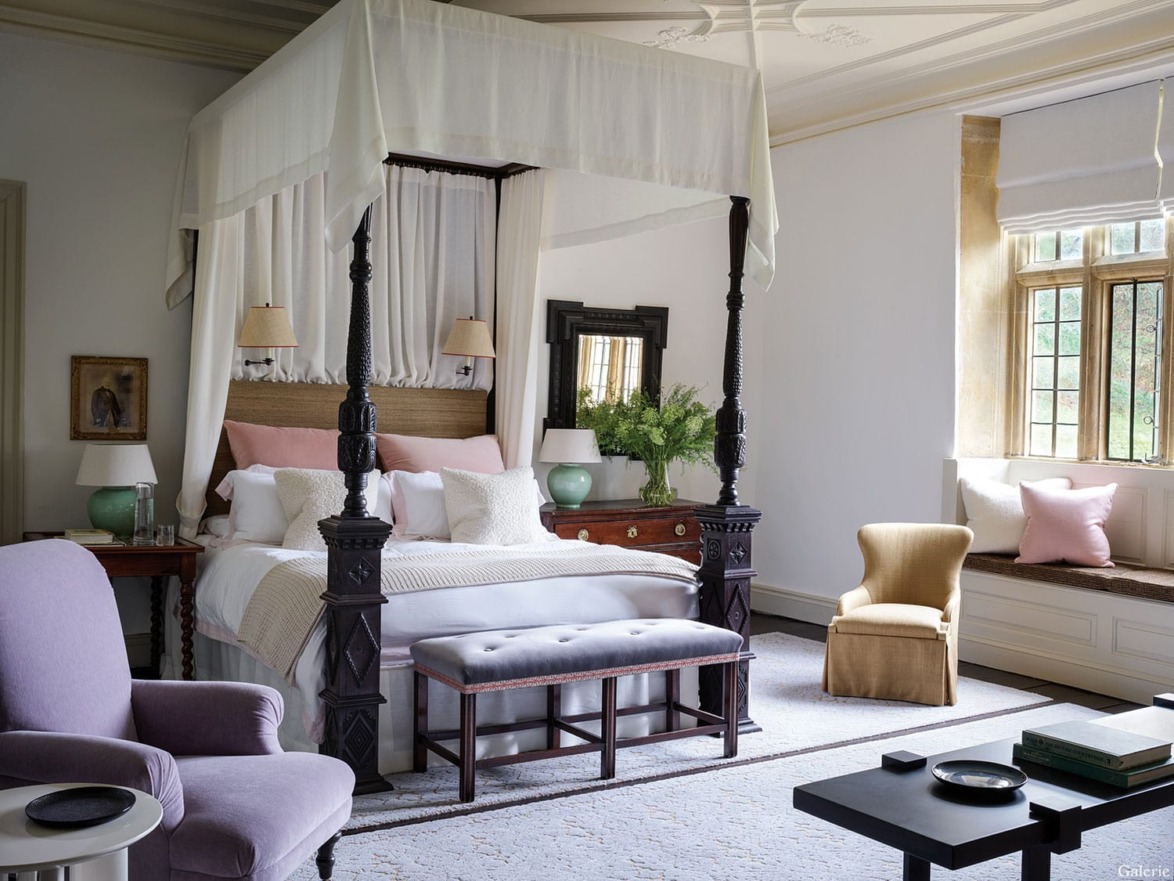 Elegant bedroom with a canopy bed, cozy seating, and large window letting in natural light. Decor includes lamps and green plants.