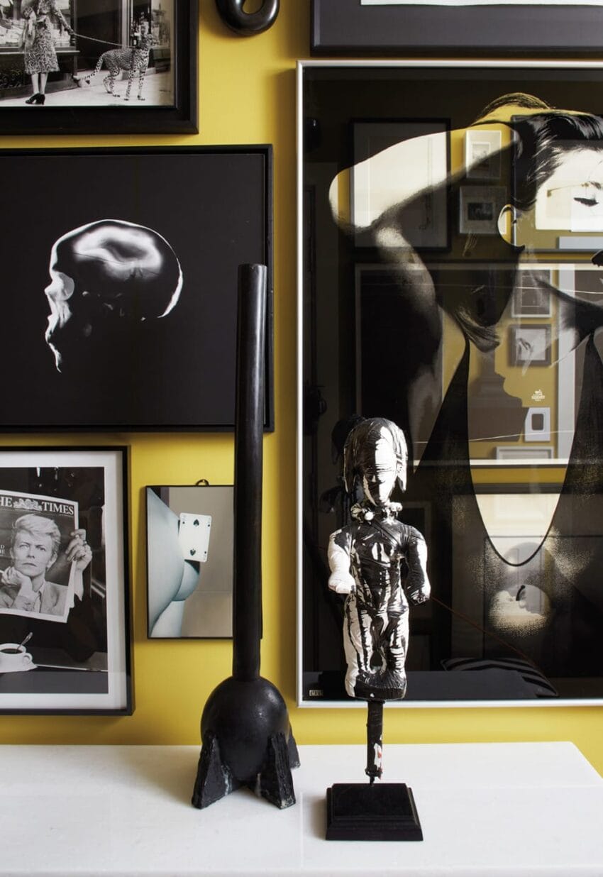 Gallery wall with various monochrome portraits and a sculptural art piece displayed on a yellow background.