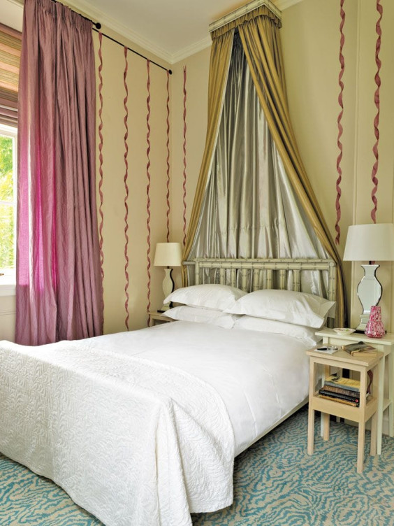 Elegant bedroom with a canopy bed, silver drapes, purple curtains, white bedding, two lamps, and a cozy blue carpet.