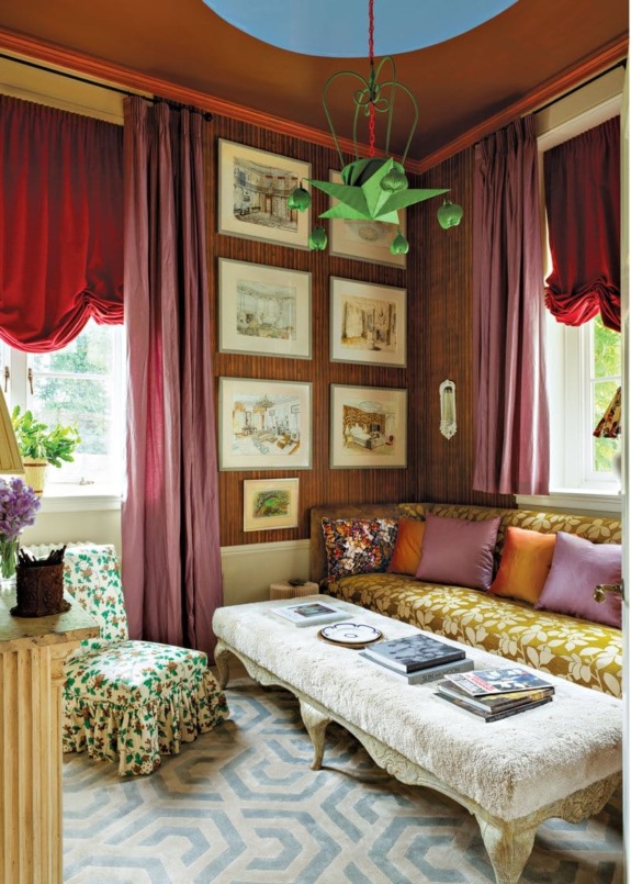 Colorful eclectic living room with patterned curtains, artwork on walls, cozy seating, and geometric rug.