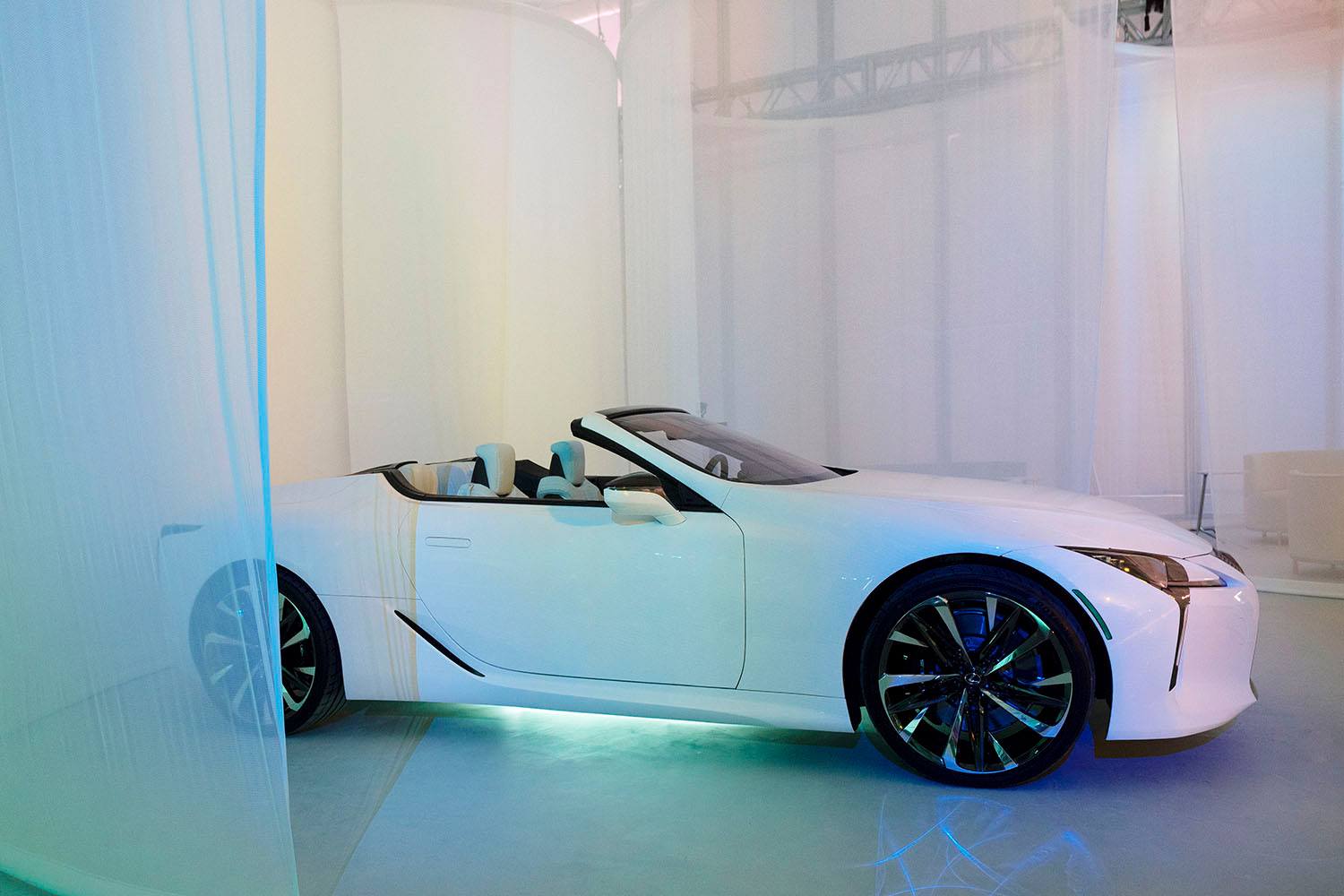 White convertible sports car displayed in a modern showroom with soft blue lighting and sleek design elements.
