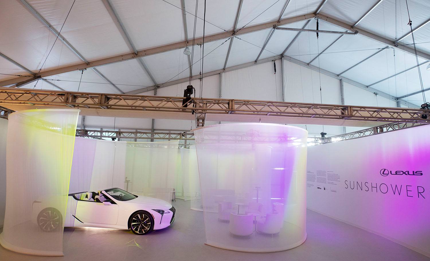 White convertible car inside a modern exhibition space with colorful lighting and large transparent curtains.