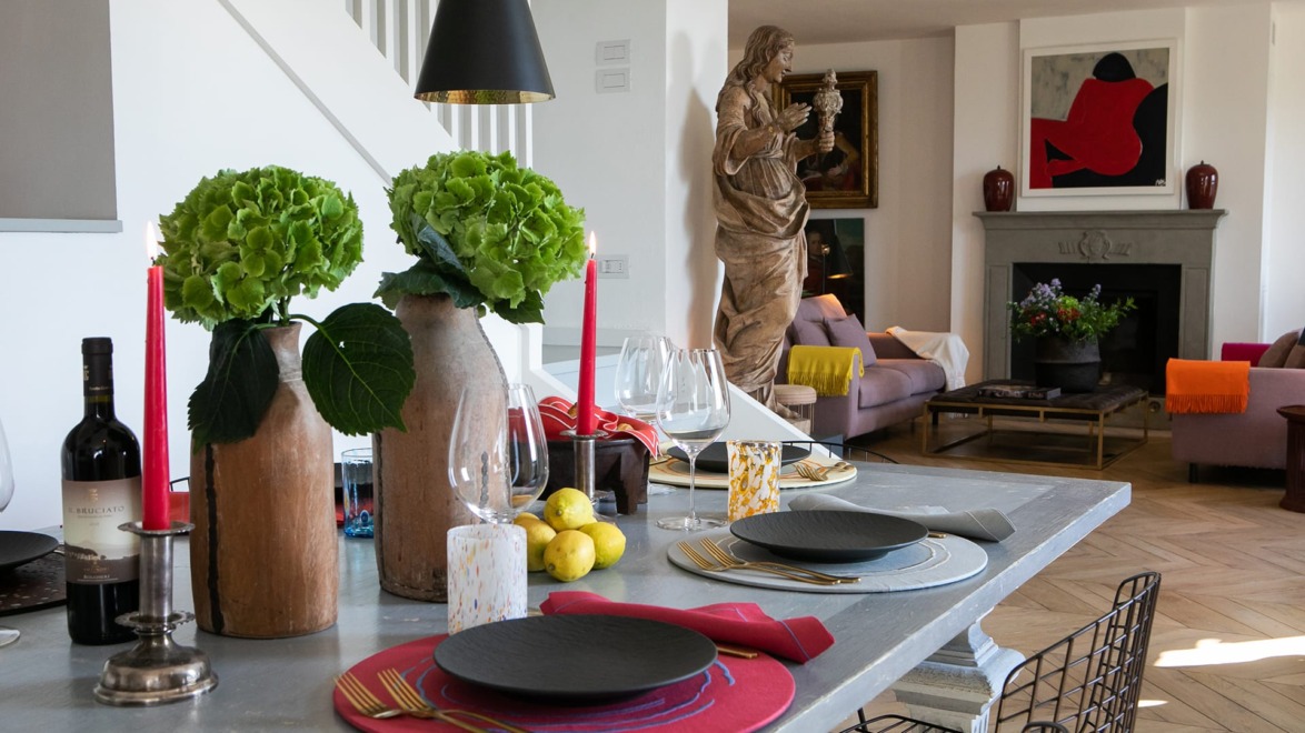 Modern dining room with a set table, decorative plants, and a glimpse into a cozy living area featuring a large statue and artwork.