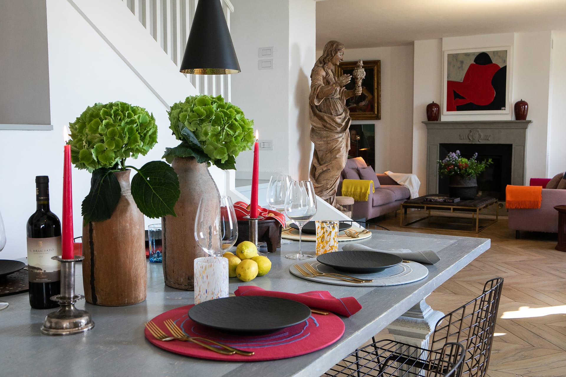 Modern dining room with a set table, decorative plants, and a glimpse into a cozy living area featuring a large statue and artwork.