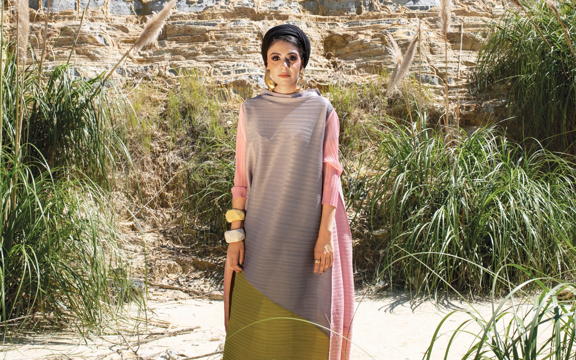 Person in a colorful dress standing outdoors in front of rocky terrain and green grasses.