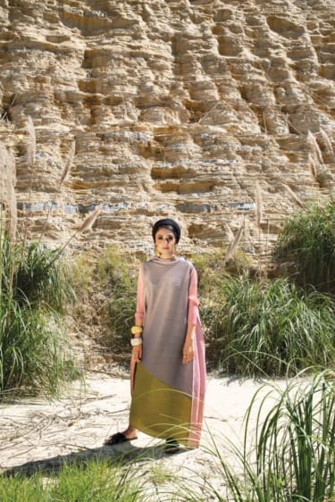 Person in colorful outfit standing in front of a rocky cliff with tall grass.