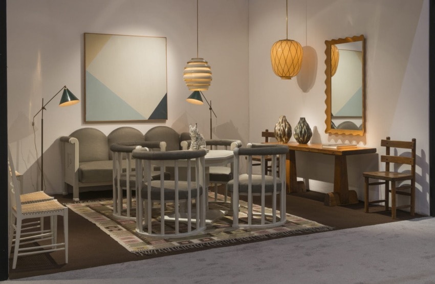 Modern living room with geometric art, gray furniture, wooden chairs, pendant lights, and a mirror on the wall.