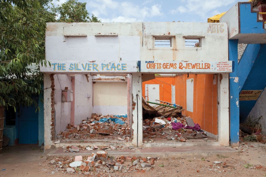 Abandoned building with debris and rubble, partial sign reads "The Silver Place," small staircase to the right, no people present.
