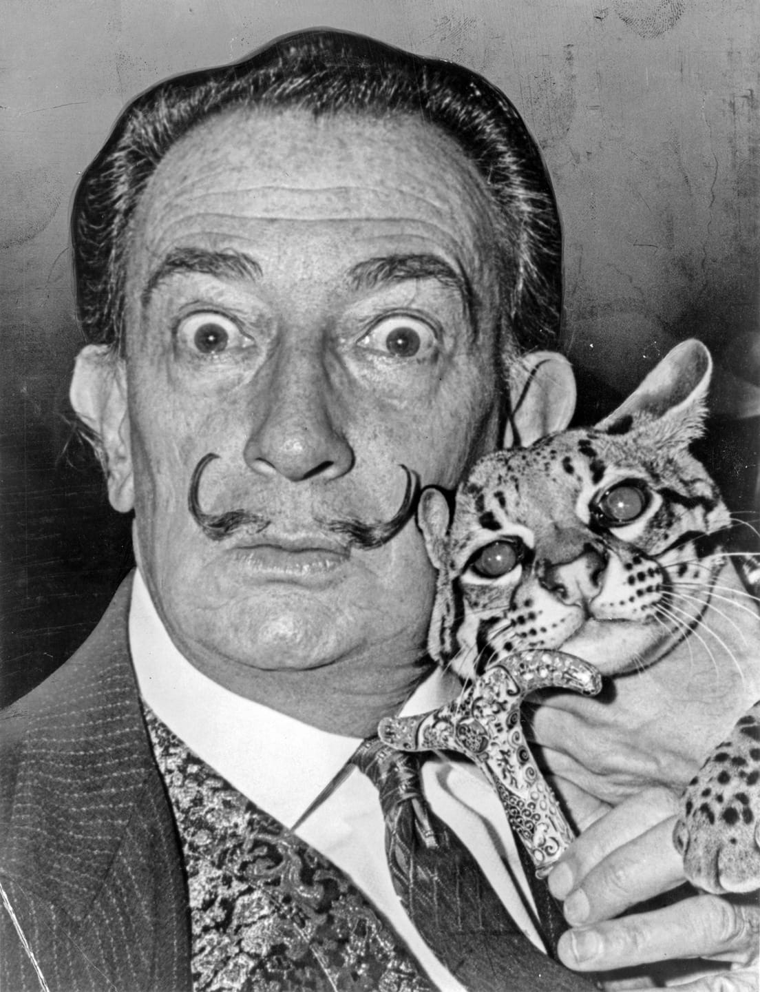 Man with a mustache holding an ocelot, both facing forward.