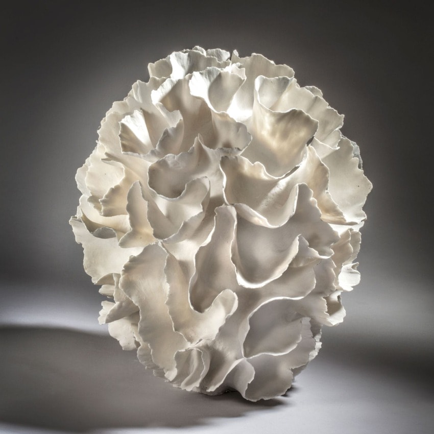 Abstract white sculpture with wavy, organic shapes resembling a blooming flower against a soft gradient background.