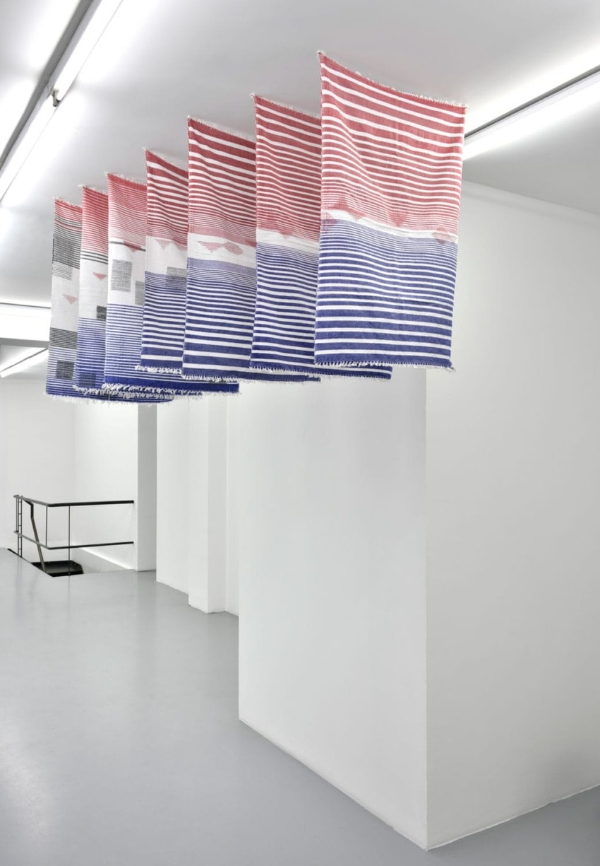 Colorful woven textiles hanging in a modern white gallery space with minimalist design elements.