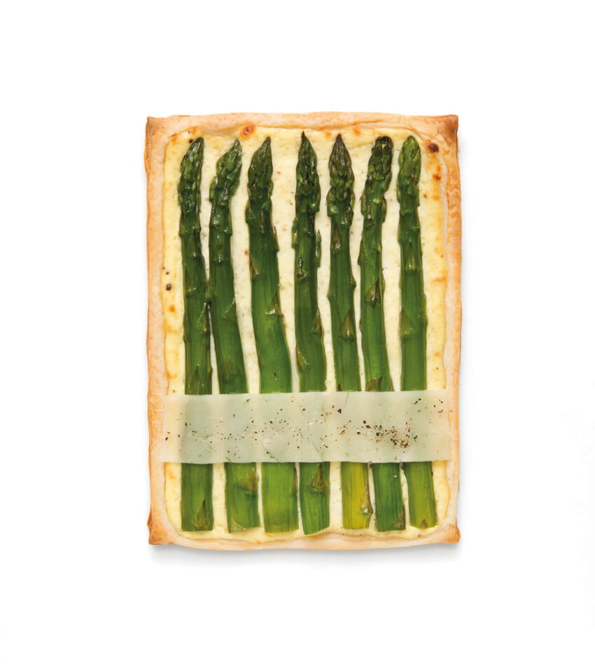 Asparagus tart with puff pastry crust and cheese slice on top, placed on a white background.