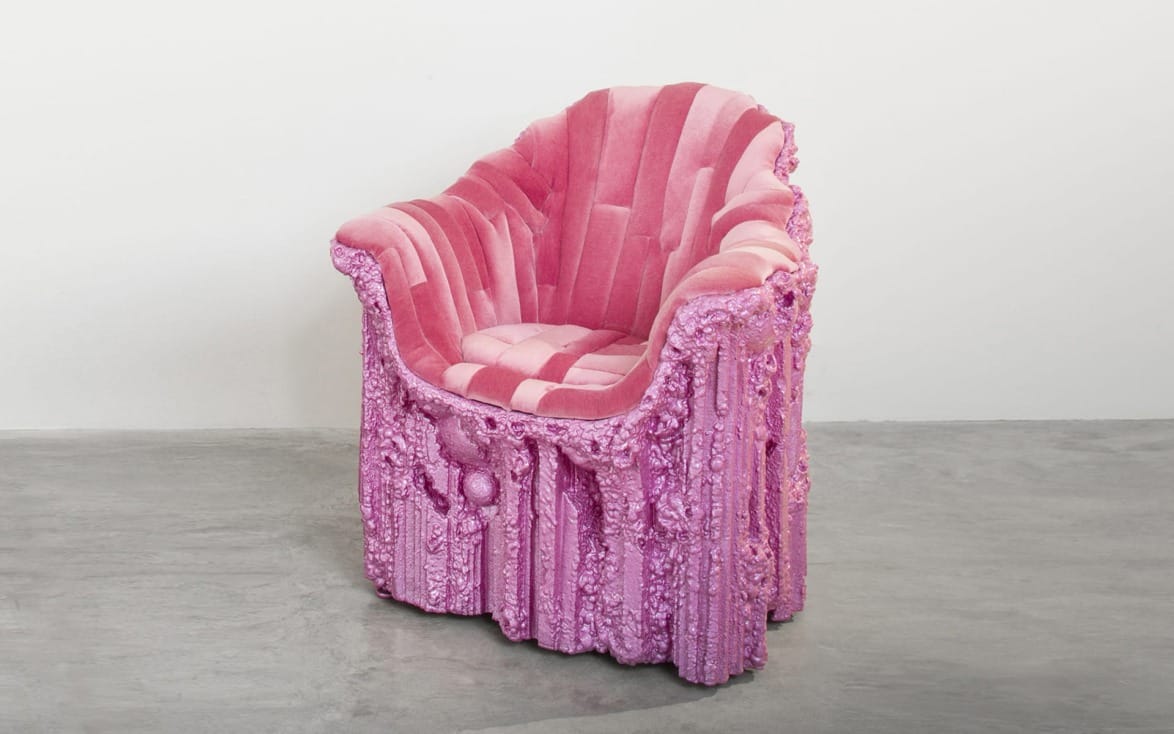 Pink, plush armchair with an ornate, textured design stands on a gray concrete floor against a plain white wall.