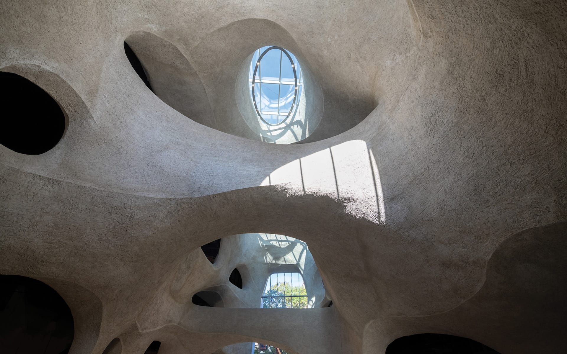 Futuristic architectural interior with curved concrete surfaces and skylight, featuring dynamic light and shadow patterns